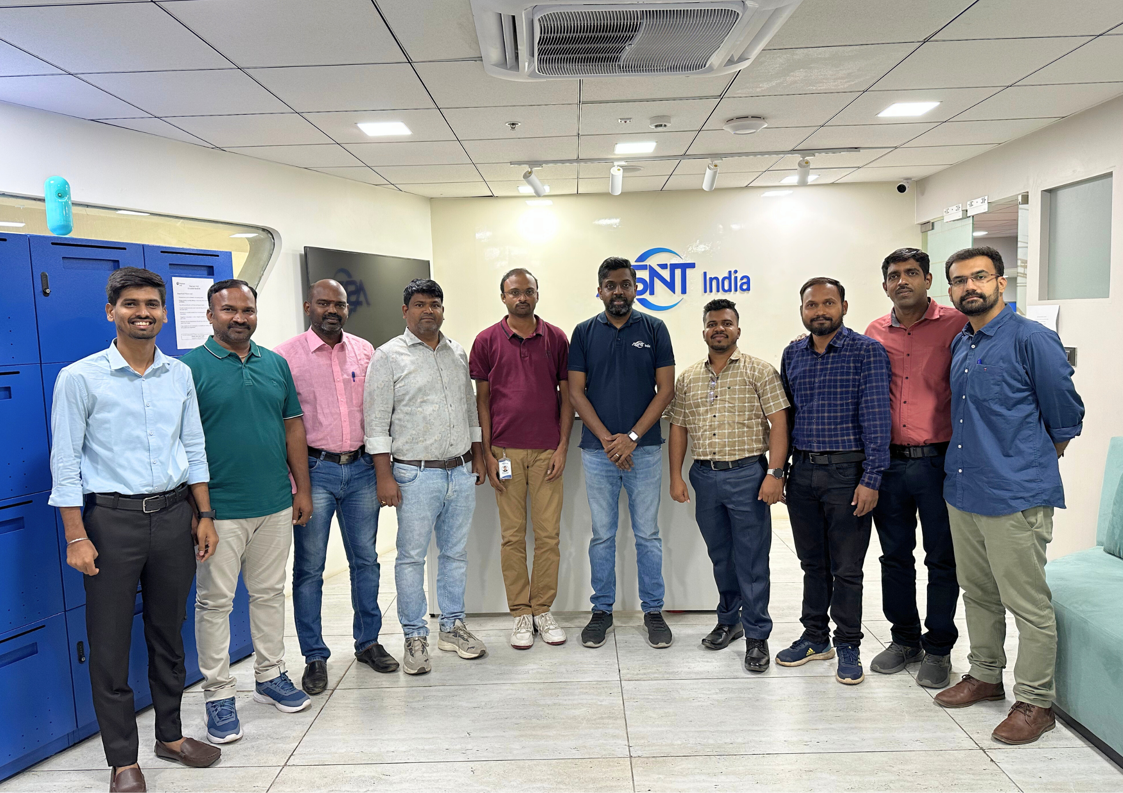 Group of eleven men standing together indoors at ASNT India office, posing for a team photo in front of a wall with the ASNT India logo.