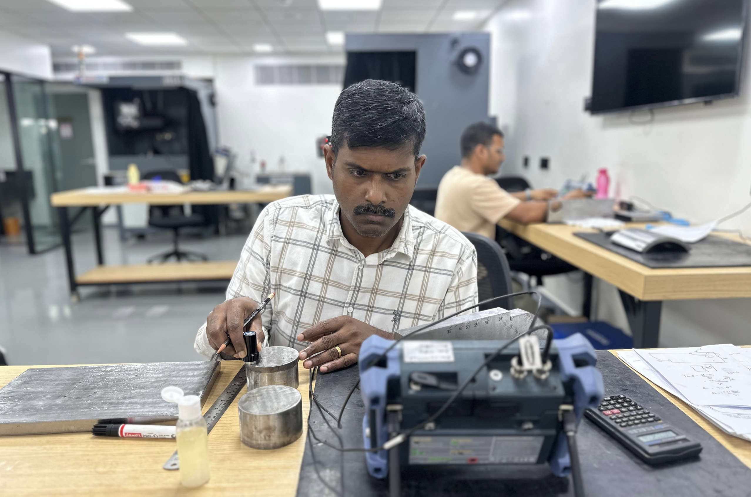 Man in a lab using an ultrasonic testing device on cylindrical metal samples, focused on calibration and measurements at a workstation."